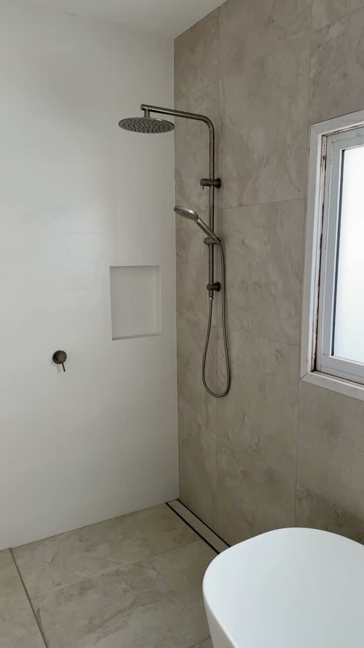 Stone-tiled walk-in shower with brushed nickel rail shower and recessed niche