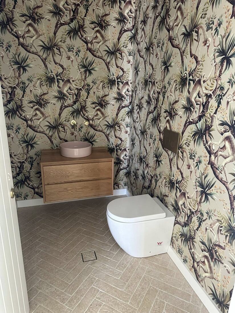 Powder room with botanical monkey-print wallpaper, oak vanity, blush basin and brass tapware