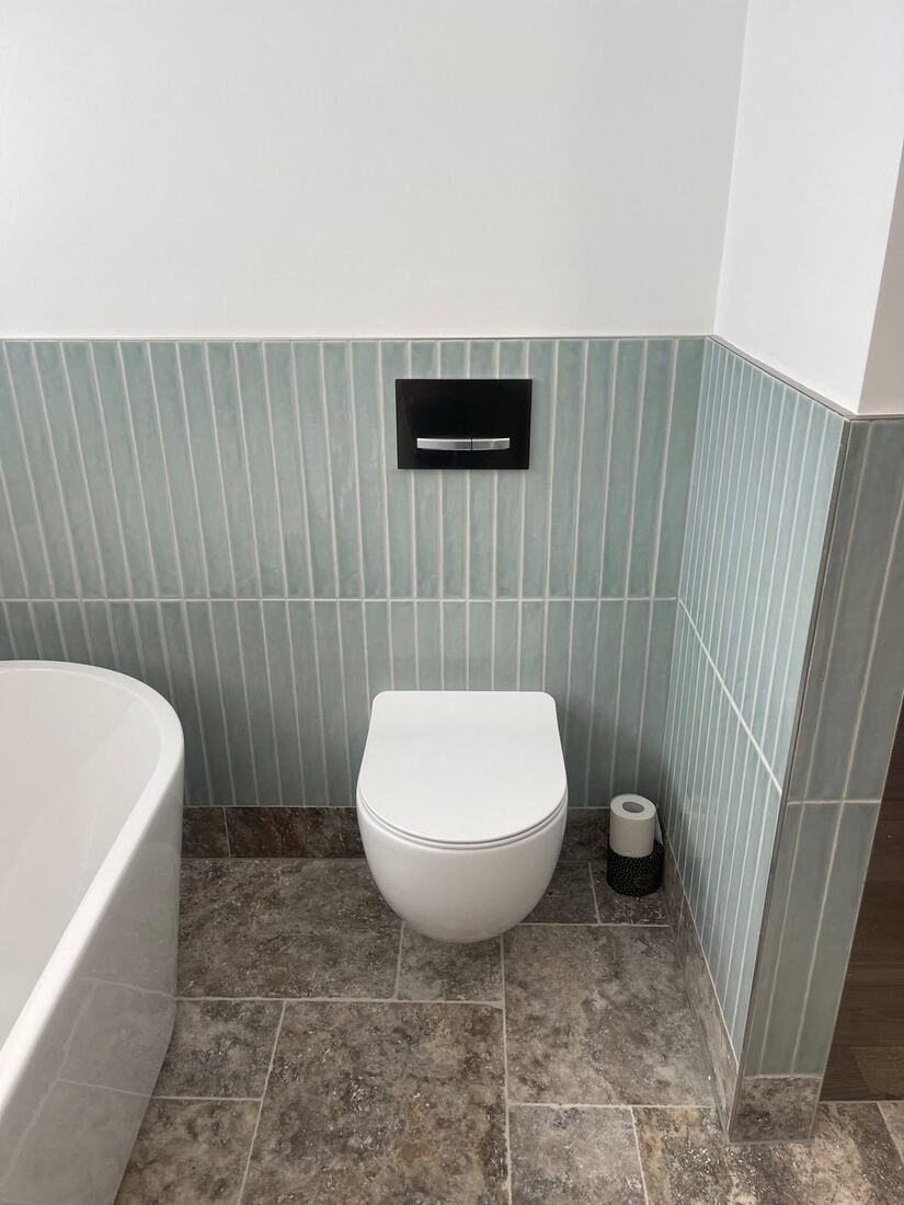 Wall-hung white toilet on vertical sage-green tile wall with travertine floor
