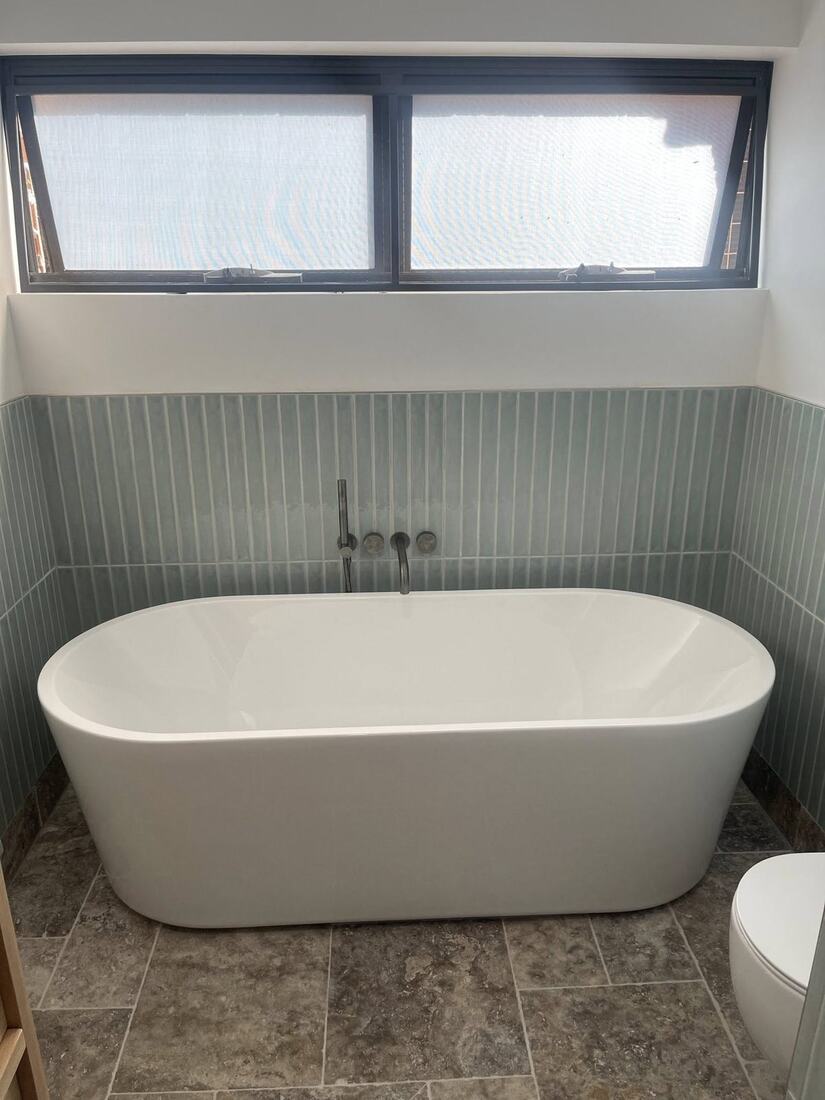 Freestanding white bath against vertical sage tile wall with chrome tap set