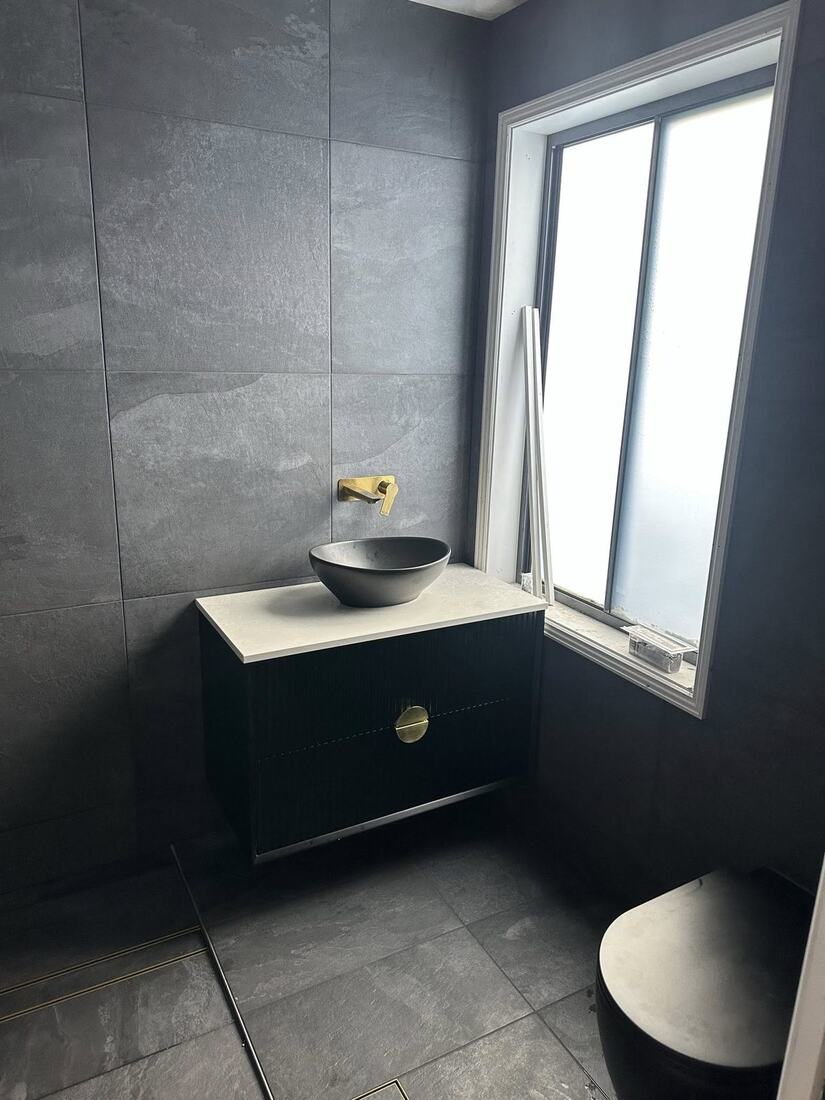 Matte black fluted vanity with concrete bowl basin and brass wall mixer on slate-grey tiled wall