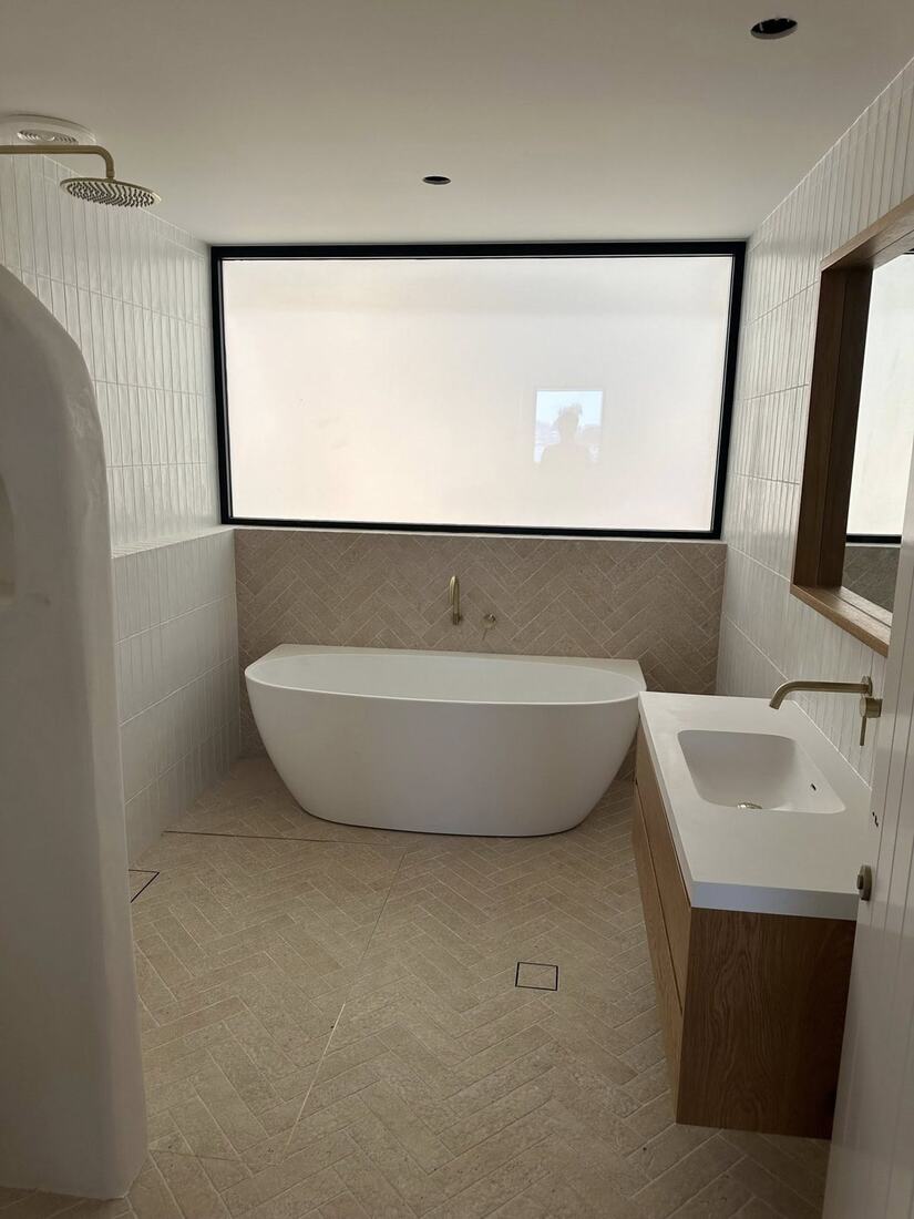 Light bathroom with herringbone travertine floor, freestanding bath and oak vanity with brushed brass tapware